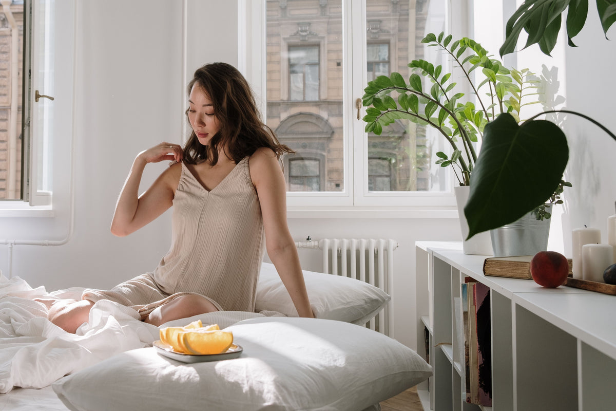 Woman sitting quietly in a bright bedroom during a reflective morning moment