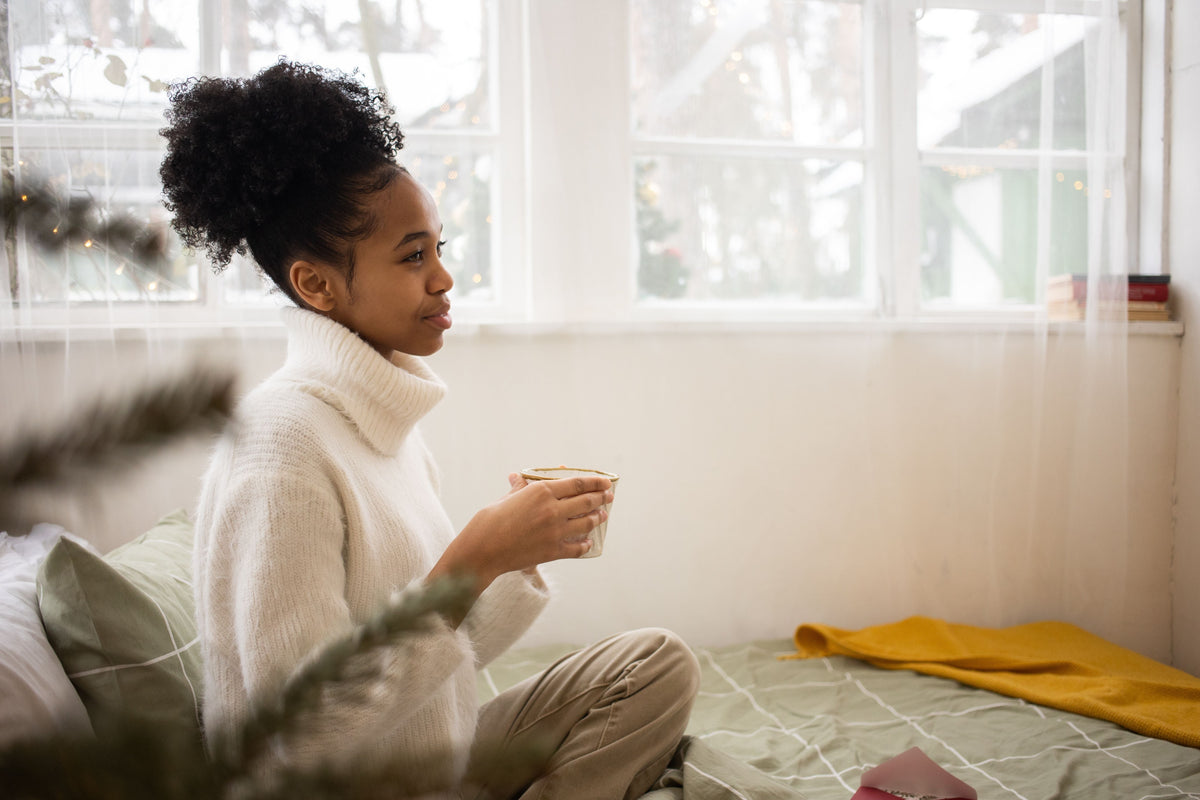 Woman sitting by a bright window holding a warm drink during a quiet New Year reset moment