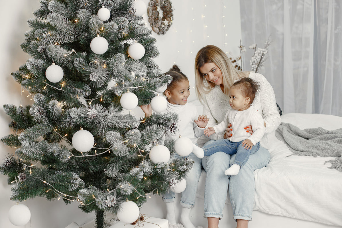 Mom sitting with her children beside a decorated Christmas tree during a cozy family holiday moment